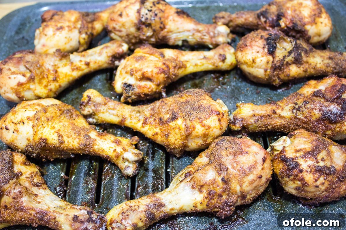Essential Solitude 3 Perfectly grilled chicken drumsticks on a broiling pan, garnished with herbs.