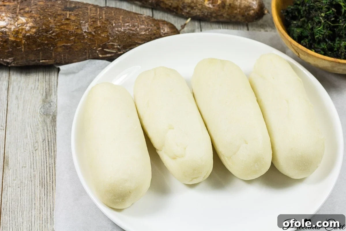 Water fufu or cassava fufu, a traditional African staple, served on a white plate alongside a vibrant soup, showcasing its smooth texture.