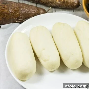 Water fufu or cassava fufu, a traditional African staple, served on a white plate alongside a vibrant soup, showcasing its smooth texture.
