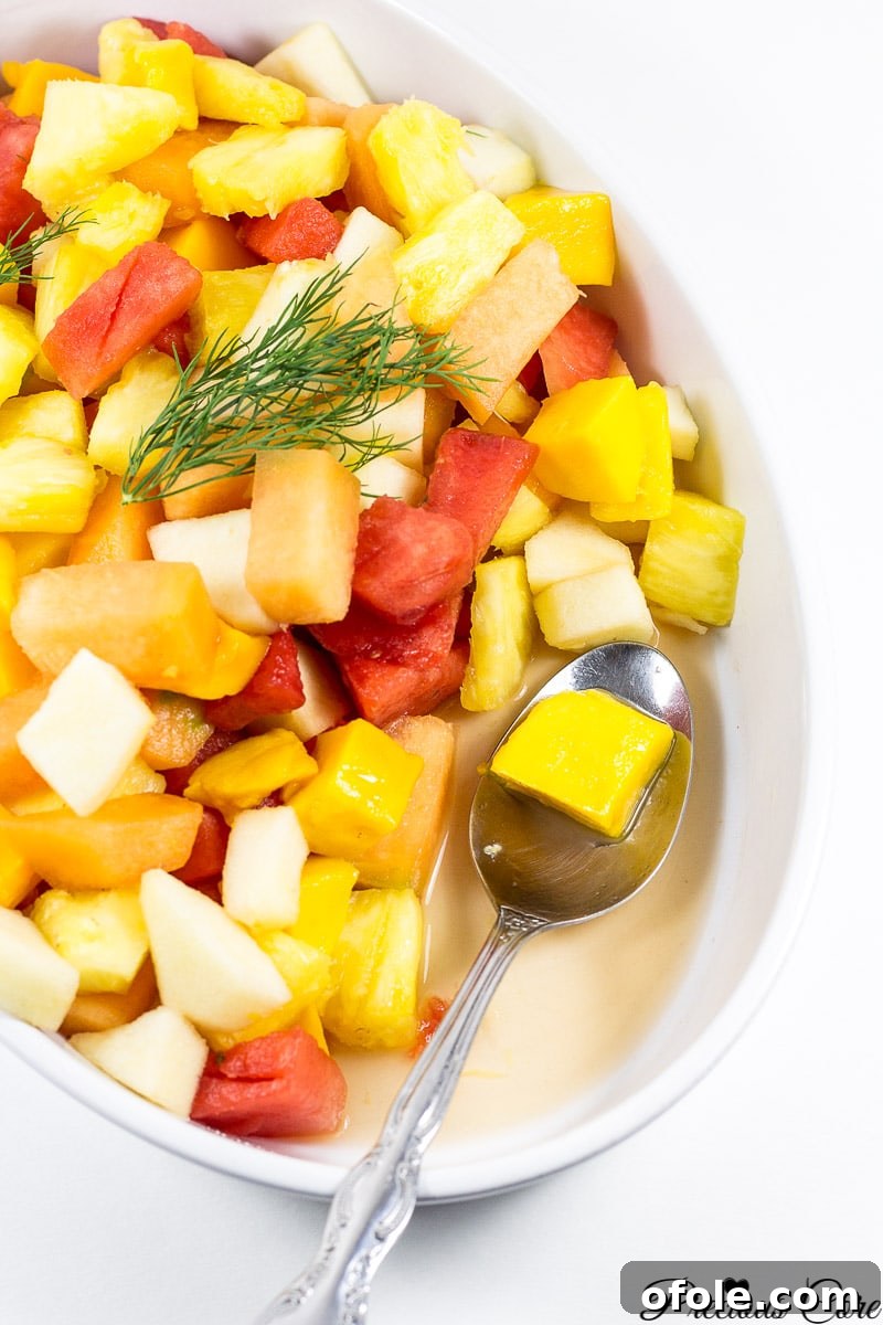 Vibrant Cameroonian Fruit Salad How To 4 A spoon delicately scooping a generous portion of colorful fruit salad from a large serving bowl, showcasing the fresh and juicy texture.