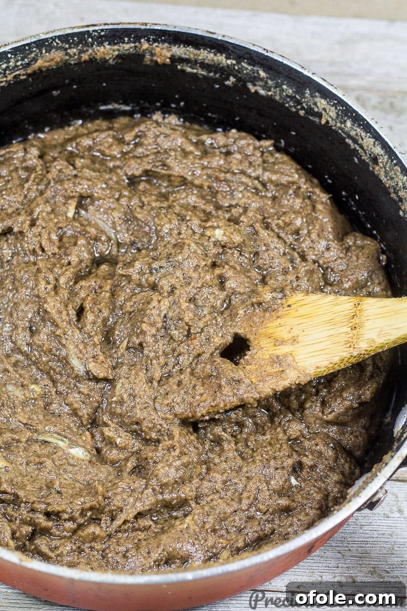 Mboh Groundnut Paste 6 A wooden spatula stirring the rich, simmering Cameroonian Mboh in a pot, showing the process of oil separation.
