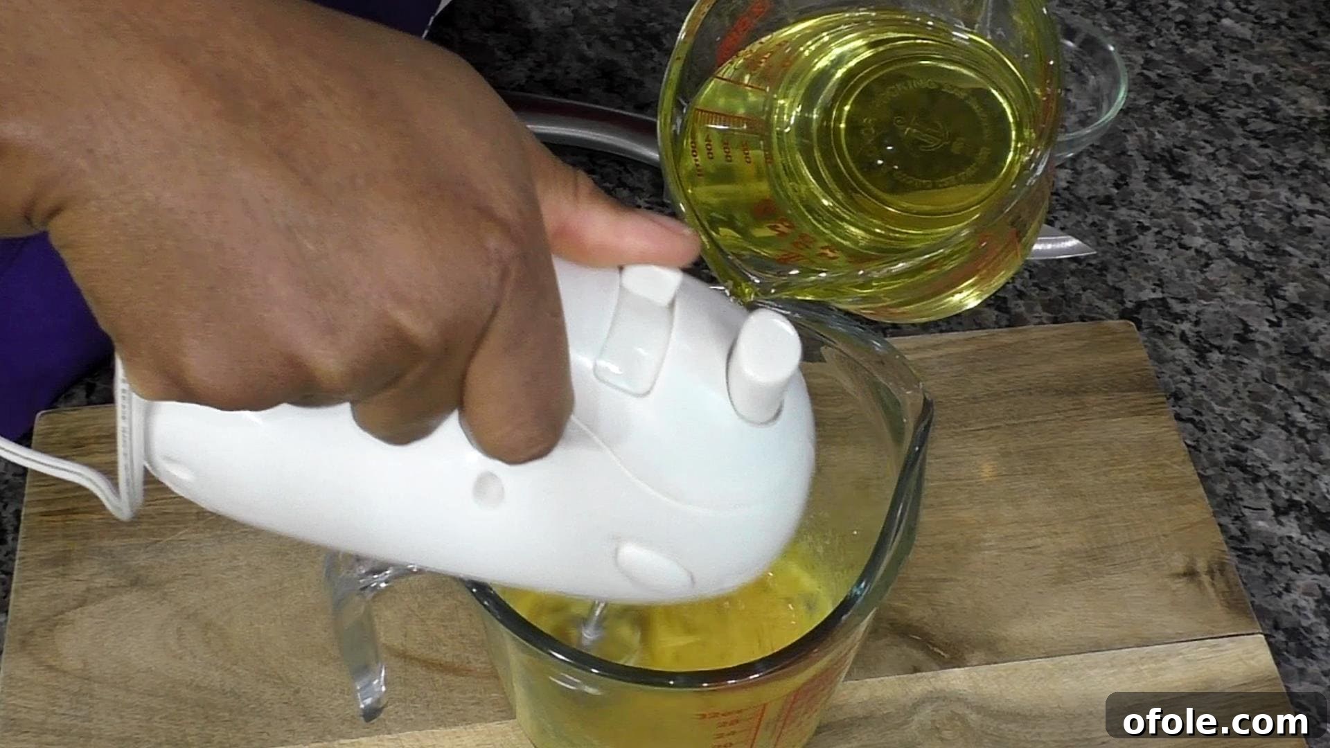 Mastering Homemade Mayonnaise 6 Hand holding hand mixer, another hand drizzling in oil to make mayonnaise