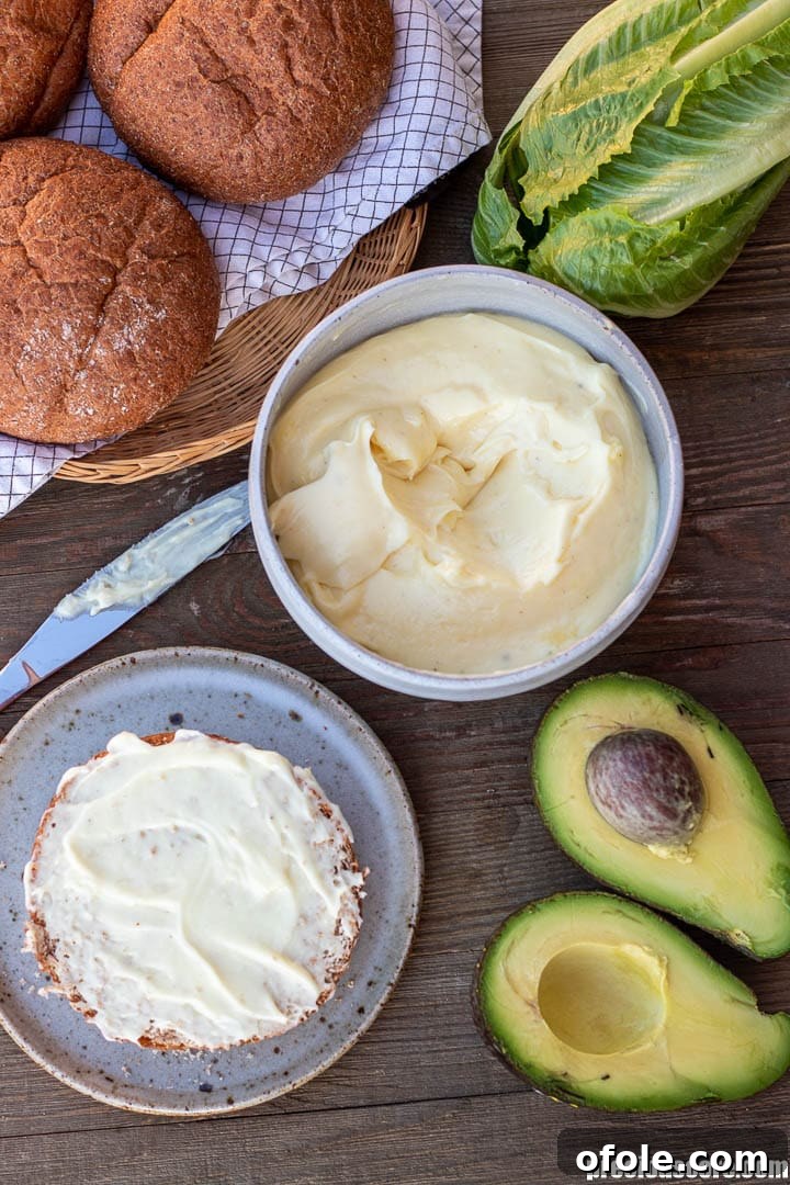 Mastering Homemade Mayonnaise 9 homemade mayoyonnaise in a bowl, bread buns in a basket, half a bun with mayo spread on top, surrounded by lettuce and avocado.