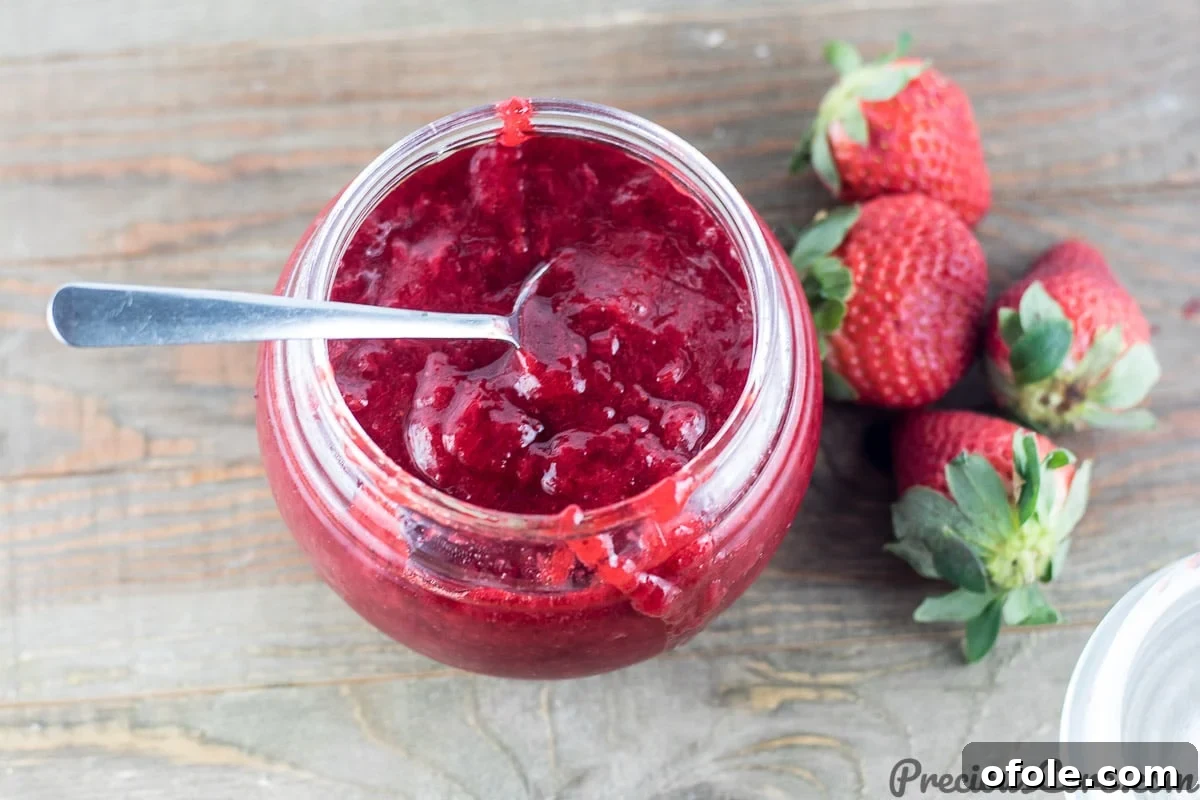 A jar of vibrant, healthy homemade strawberry jam on a rustic surface.