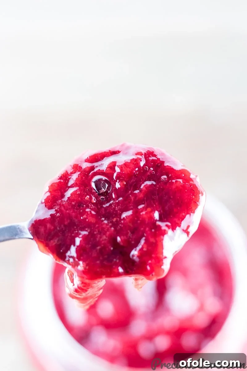 A spoon scooping luscious healthy strawberry jam from a jar.