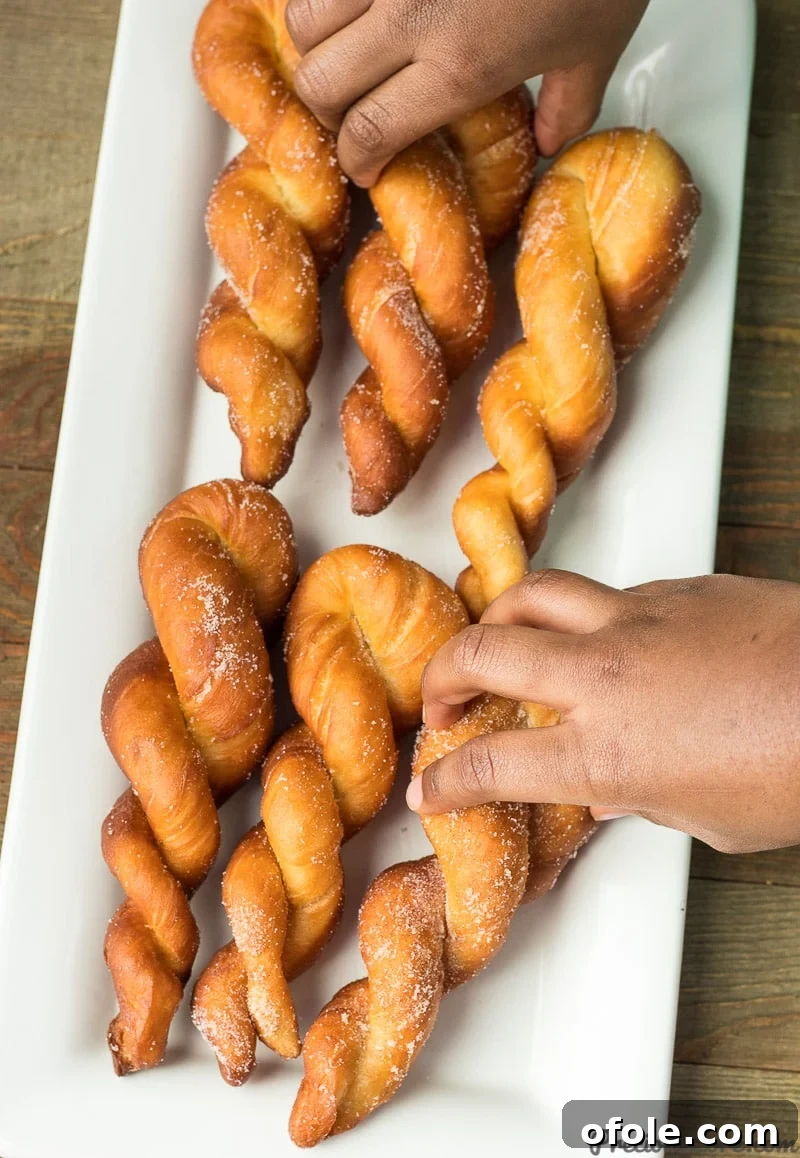A hand reaching for a freshly fried and sugared African twisted doughnut.