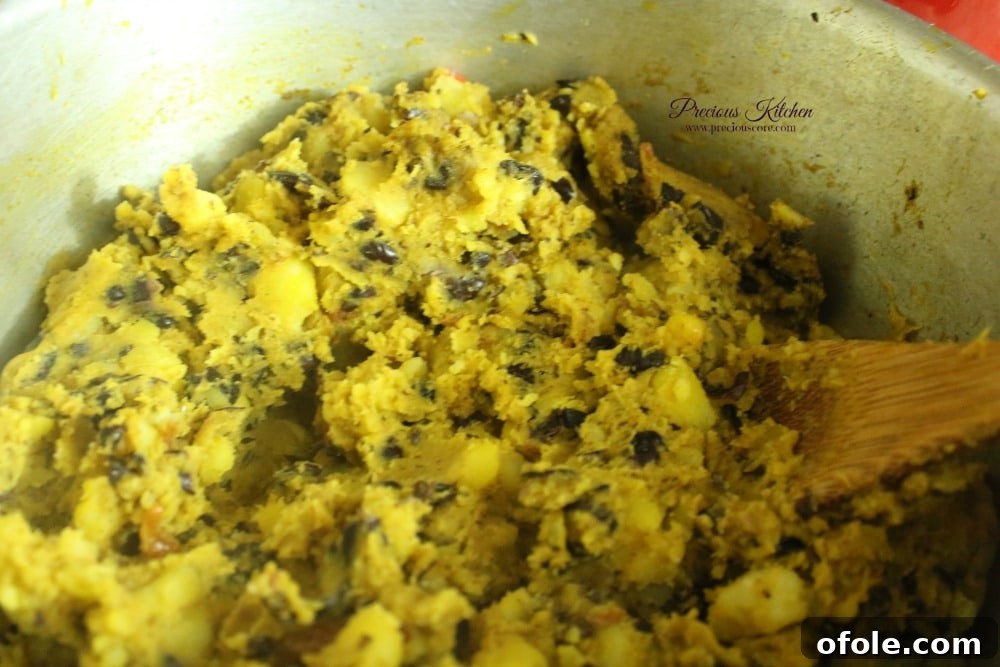 A cook expertly mashing the potatoes and beans together in the pot with a wooden spoon.