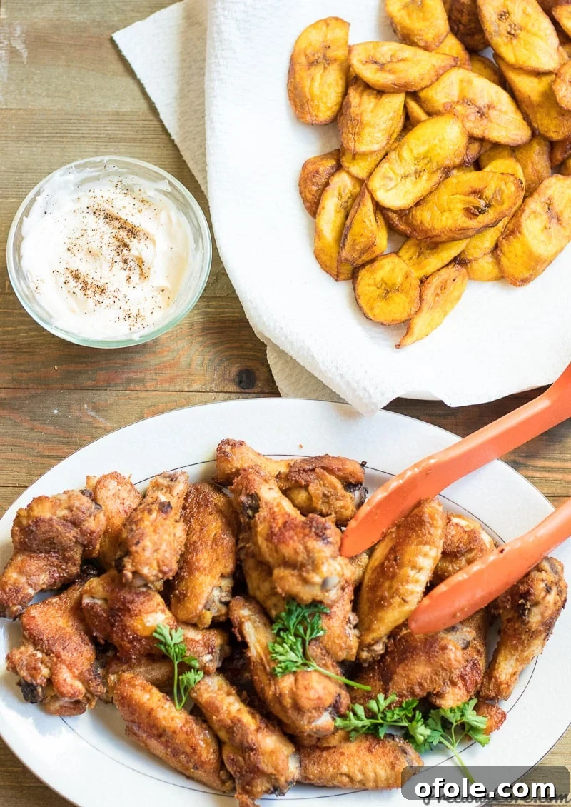 Oven-grilled chicken wings served with sweet fried plantains and herby mayo, showcasing their crispy texture and delicious golden-brown crust.
