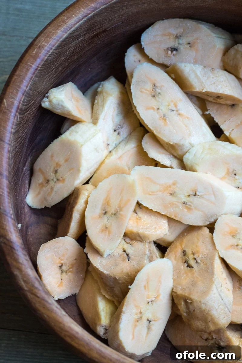 Golden Caramelized Plantains 4 Neatly cut diagonal slices of sweet plantains, ready for frying, gathered in a wooden bowl.