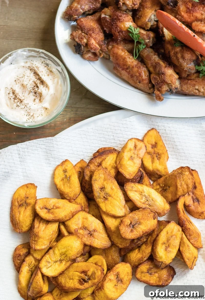 Golden Caramelized Plantains 6 A delicious meal featuring golden fried plantains served alongside crispy chicken wings on a white plate.