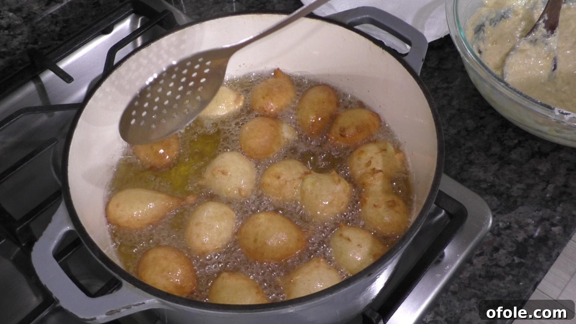 Golden Banana Bites 8 Several banana fritters happily deep-frying in hot oil within an enameled cast iron pot, turning golden brown.