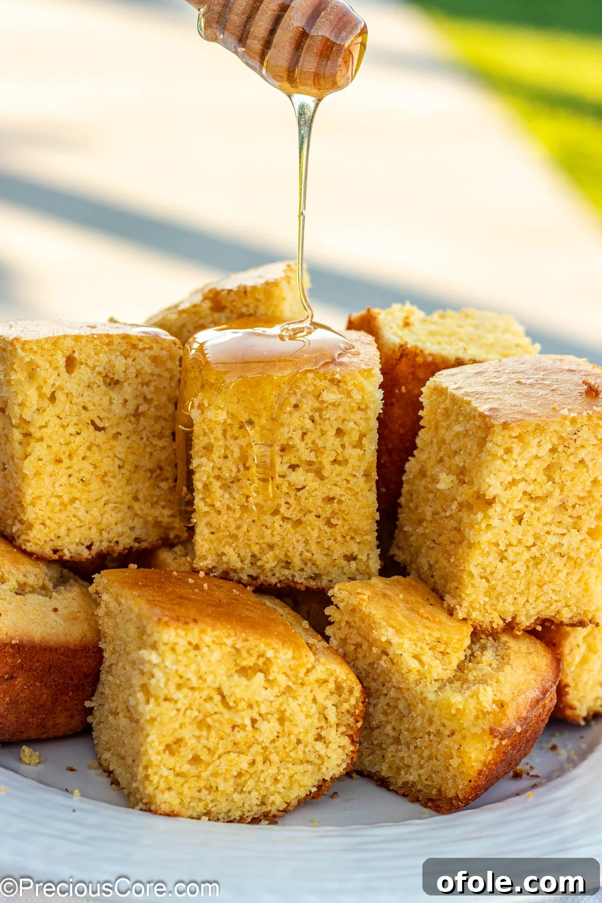 Golden square slices of cornbread without buttermilk, glistening with honey drizzled on top, arranged artfully on a rustic surface.