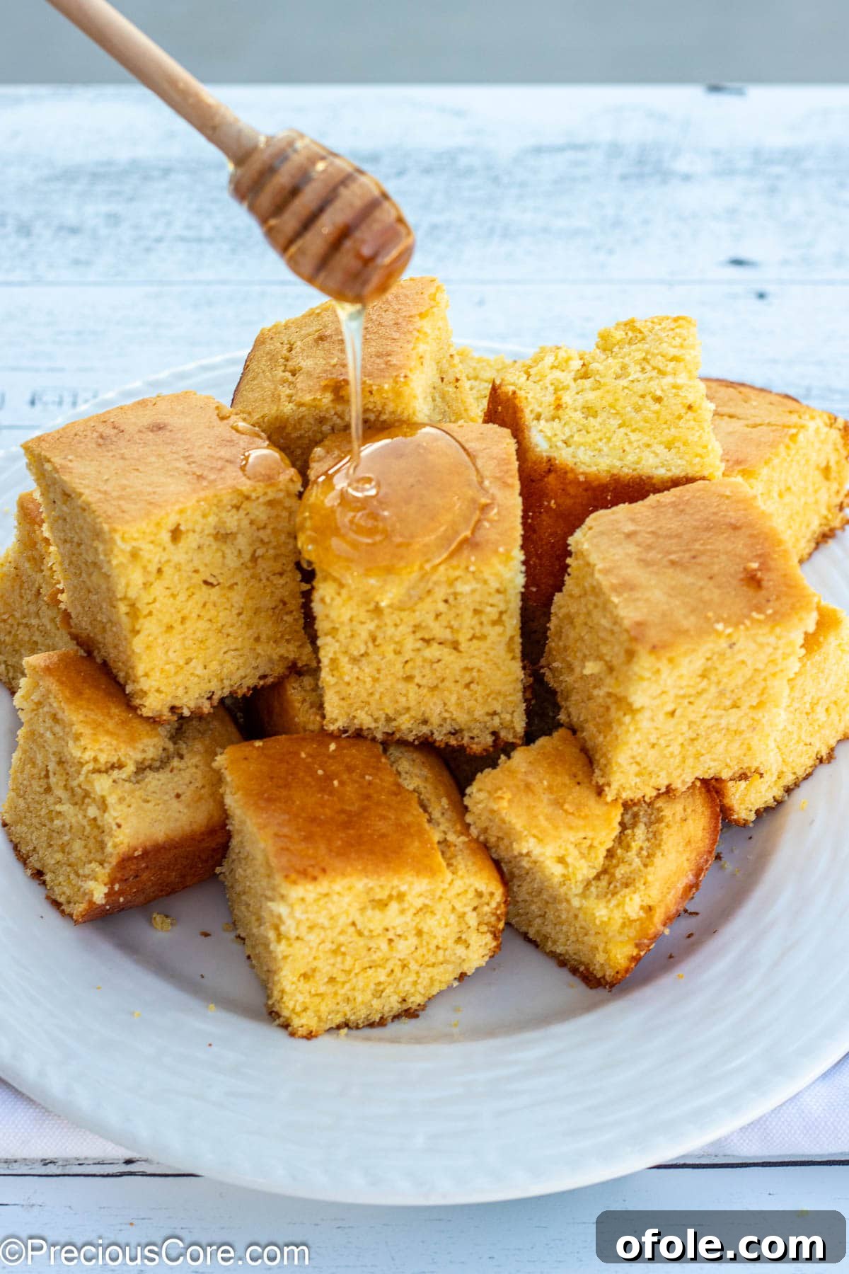 A honey wand gracefully drizzling golden honey over warm slices of cornbread.