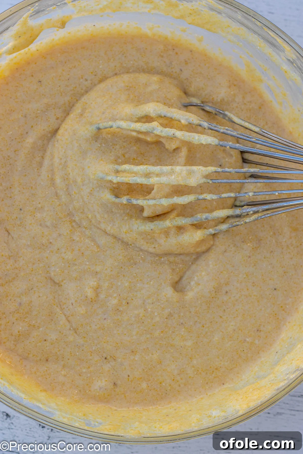 Thick, golden cornbread batter with a whisk, resting in a large mixing bowl.
