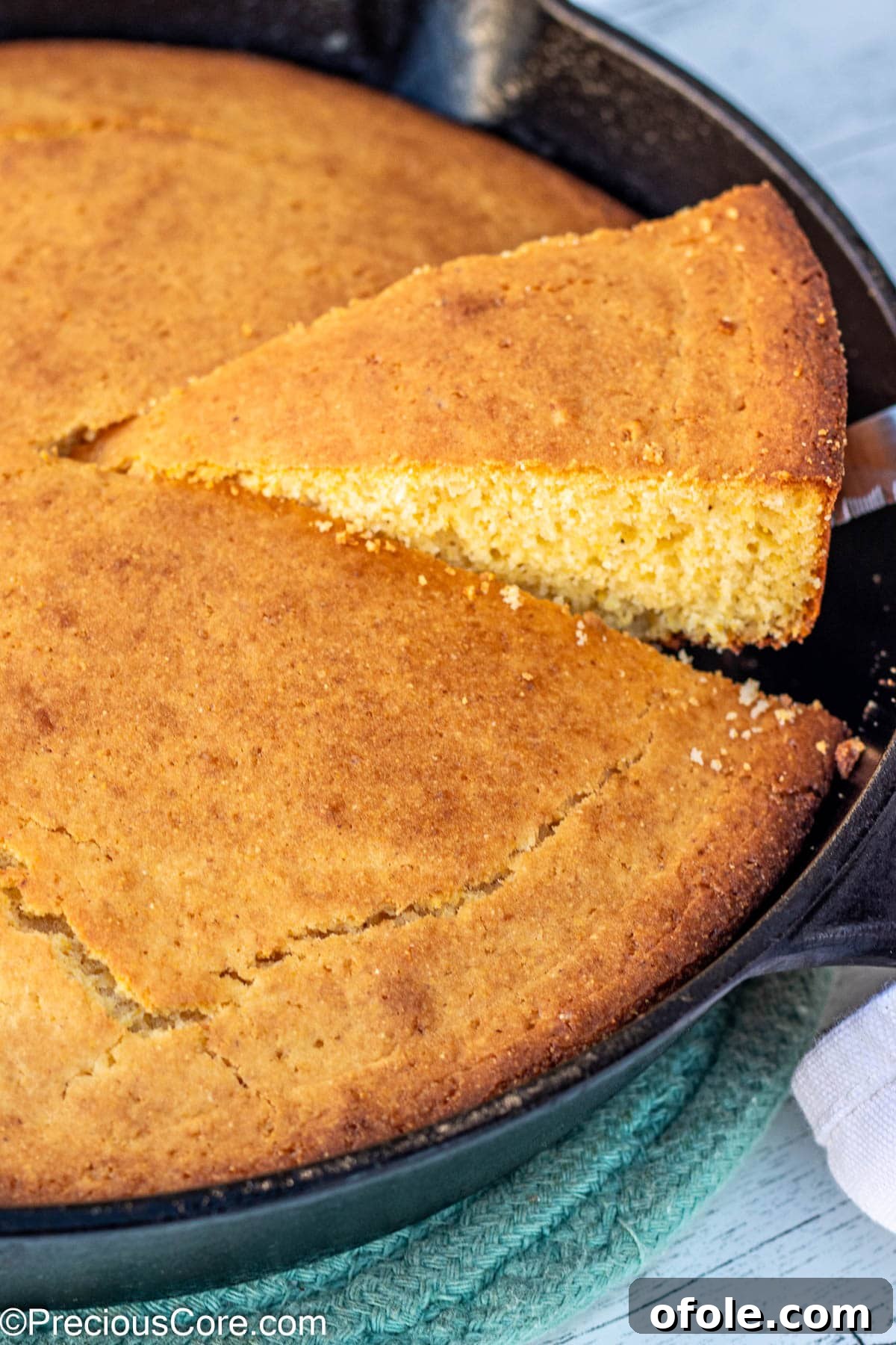 A slice of warm cornbread being carefully lifted from a cast iron skillet, steam gently rising.
