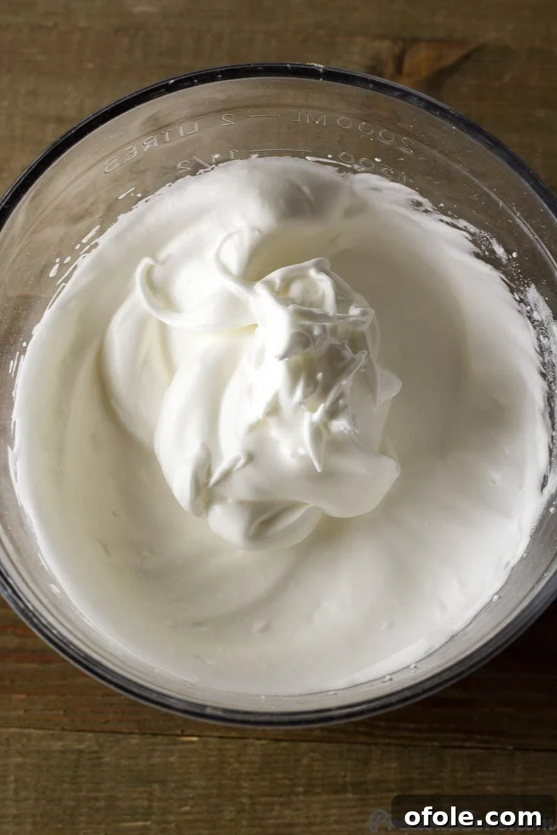 Fluffy Vanilla Cake 4 A pristine glass bowl filled with perfectly whipped egg whites, exhibiting firm, stiff peaks, ready to be incorporated into the delicate vanilla sponge cake batter.