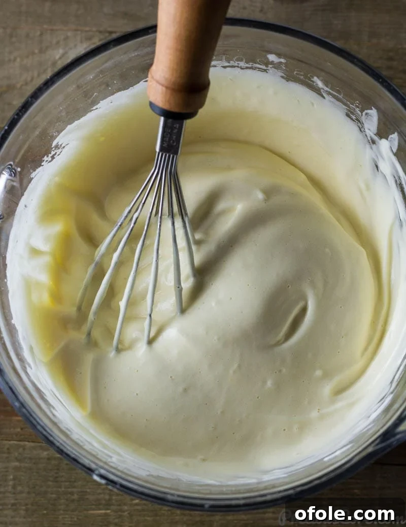 Fluffy Vanilla Cake 5 A whisk delicately stirring egg yolks and fragrant vanilla extract into a bowl of light, fluffy whipped egg whites, creating the essential base for a flawless sponge cake.