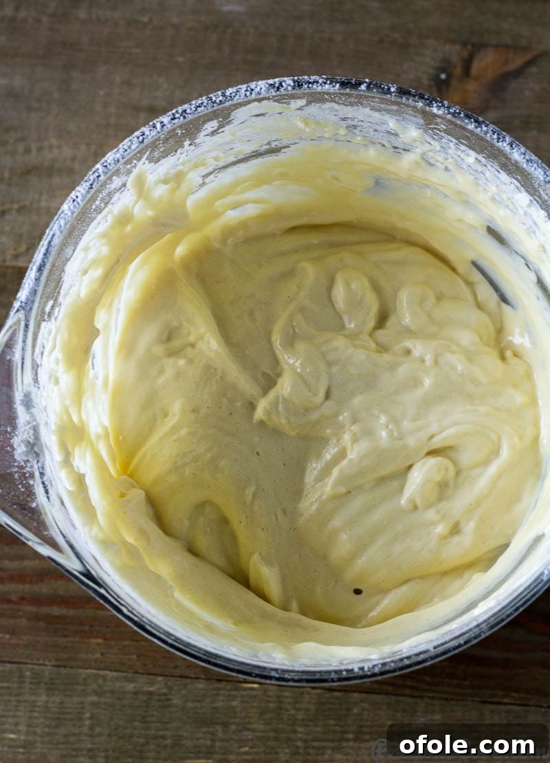 Fluffy Vanilla Cake 6 A beautifully smooth, pale yellow vanilla sponge cake batter nestled in a glass mixing bowl, showcasing its light, airy, and uniform consistency, ready for the baking pan.