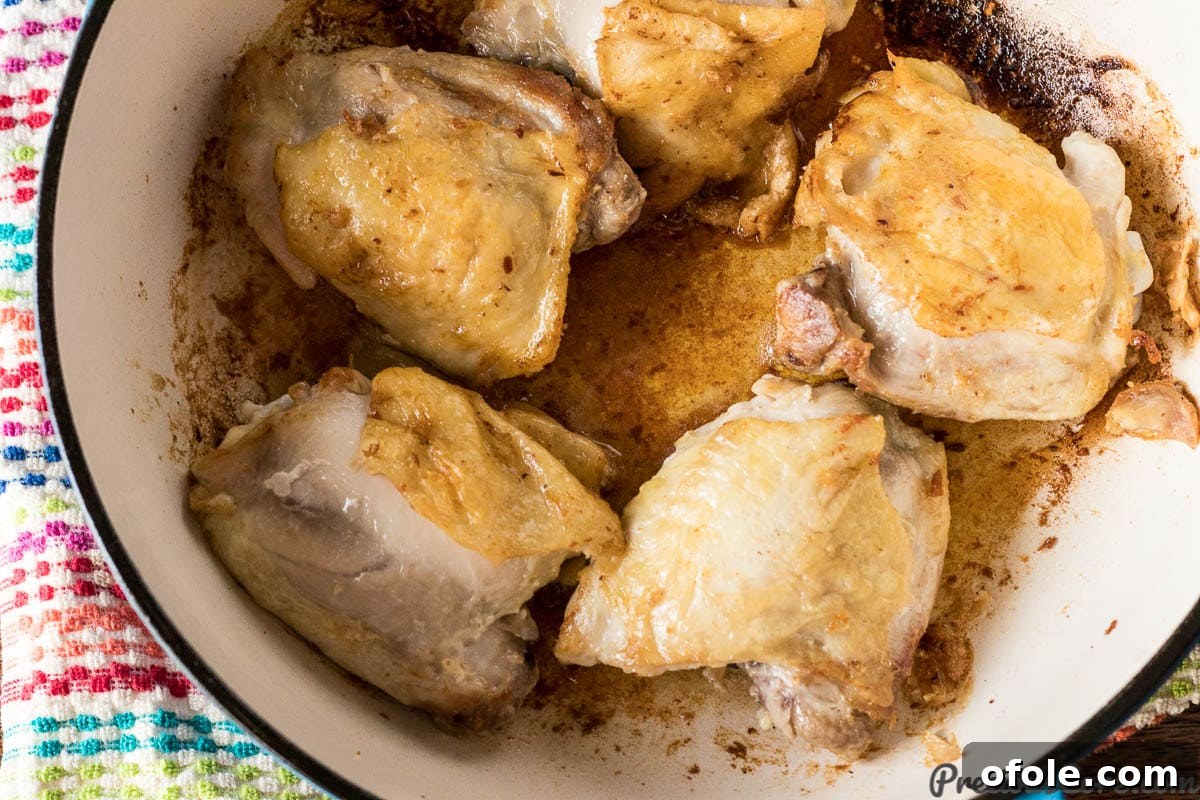 Searing chicken thighs in a hot pan to develop a golden crust.