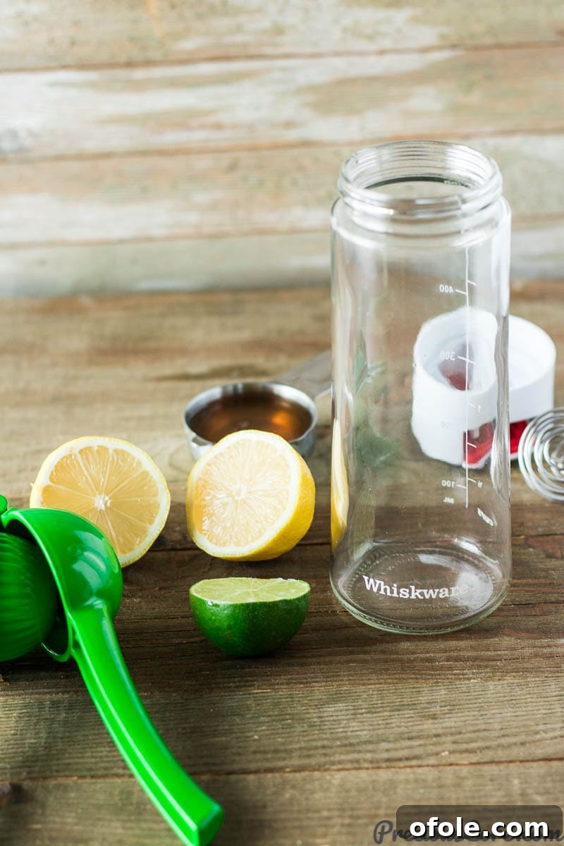 A Whiskware dressing shaker filled with honey citrus dressing, surrounded by fresh citrus halves and a honey jar.