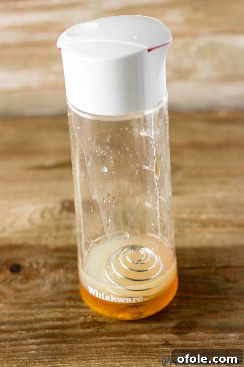 A Whiskware dressing shaker holding a vibrant golden citrus honey dressing, ready to be poured.