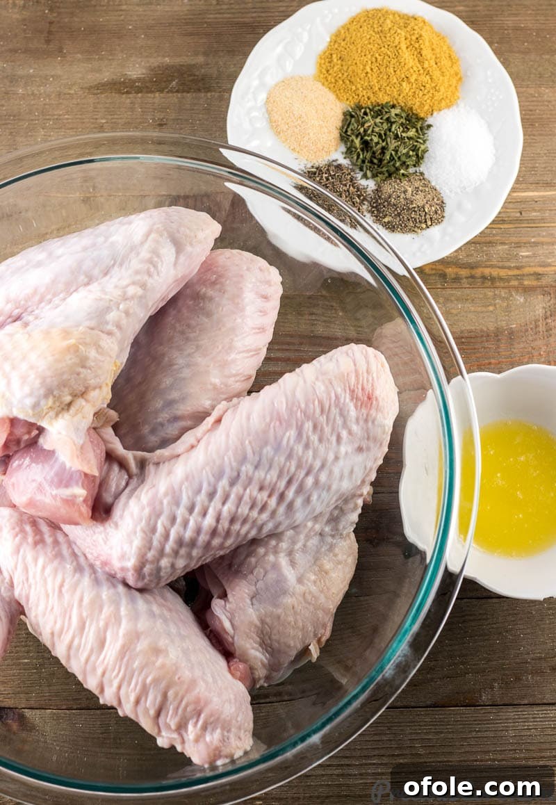 Golden Baked Turkey Wings 4 Fresh turkey wings in a bowl, a selection of spices and herbs on a plate, and melted butter in a small bowl, all laid out for preparation.