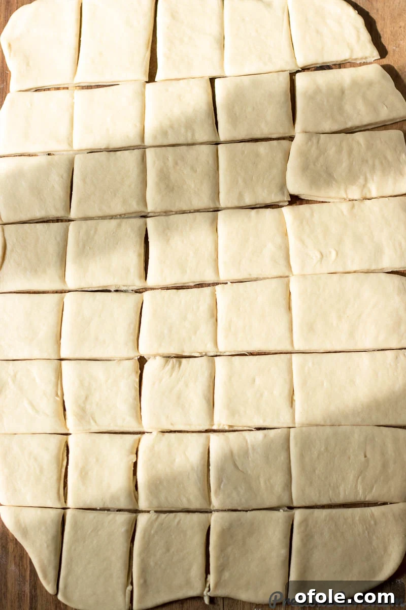 Beignet dough neatly cut into uniform squares on a wooden surface, ready for frying.