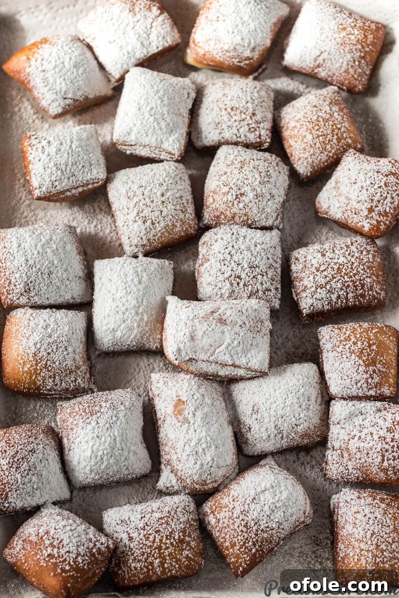 A baking sheet full of cooked beignets, heavily dusted with a cloud of powdered sugar.