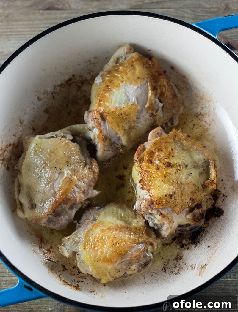 Golden brown chicken pieces sizzling in a cast iron pot, ready for the stew