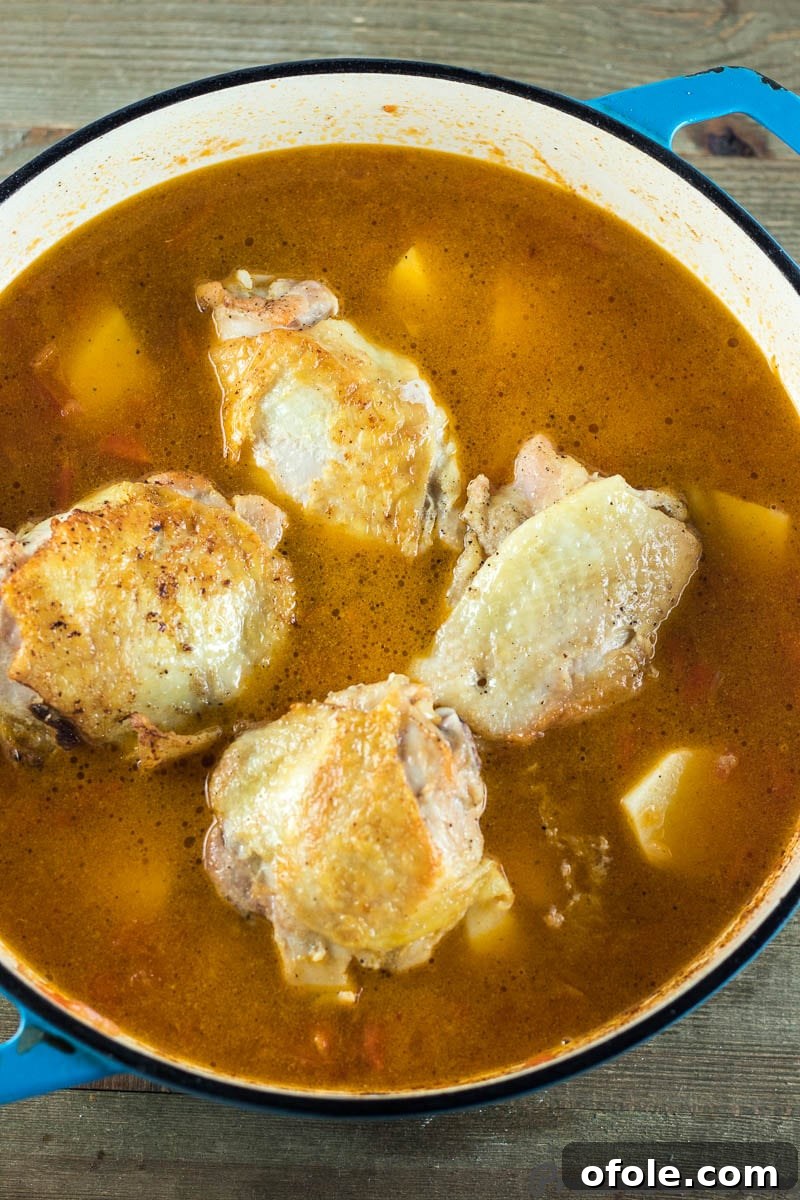 Chicken and Potatoes simmering in a rich, red tomato broth inside a cooking pot