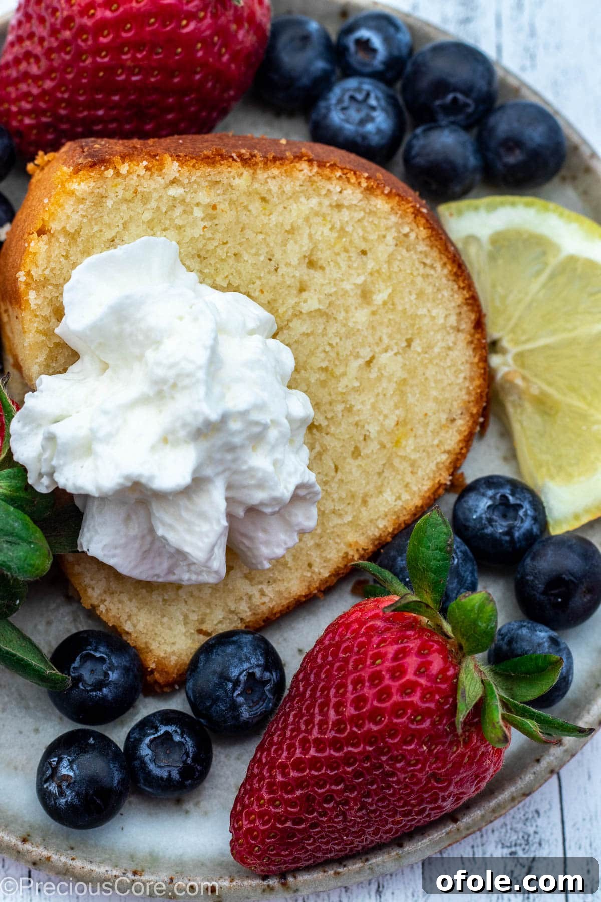 Zesty Southern Lemon Pound Cake 3 A delectable slice of lemon pound cake on a white plate, elegantly topped with a dollop of whipped cream and garnished with fresh mixed berries.