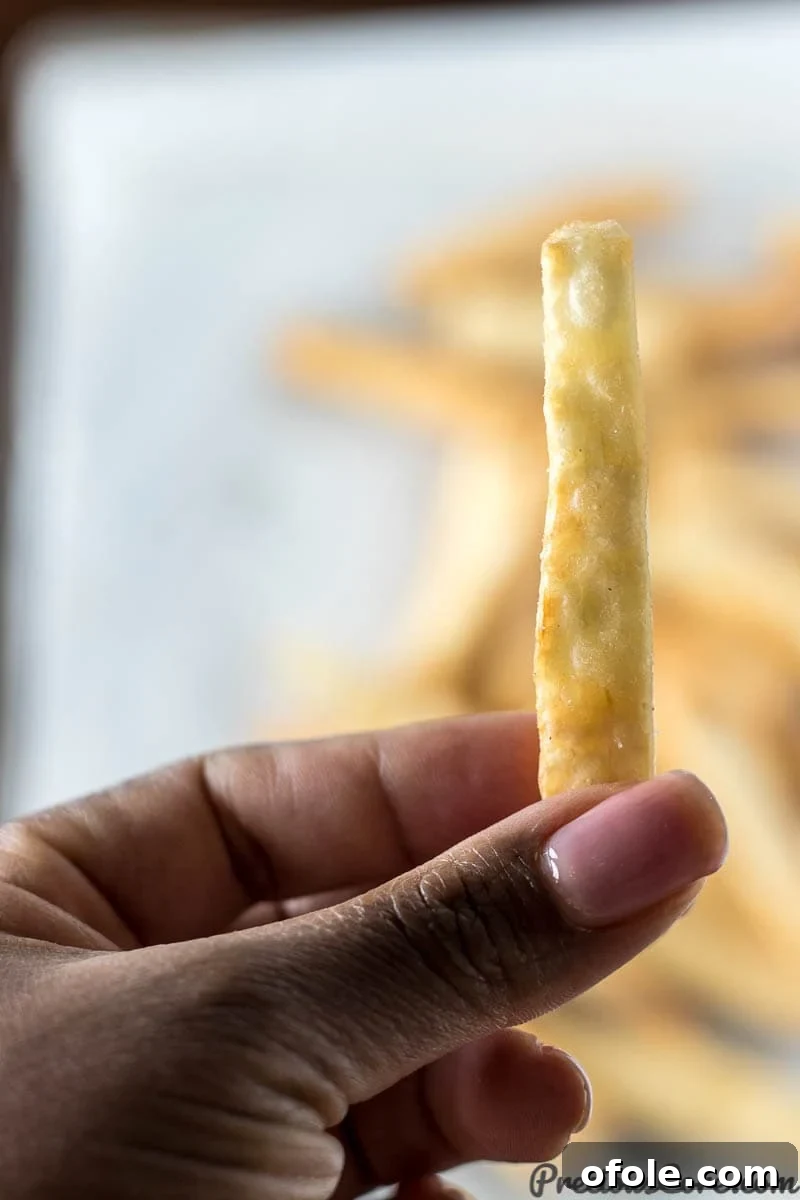 Golden Crunchy Yuca Fries 3 A hand holds a single, perfectly crispy yuca fry, showing its golden texture.