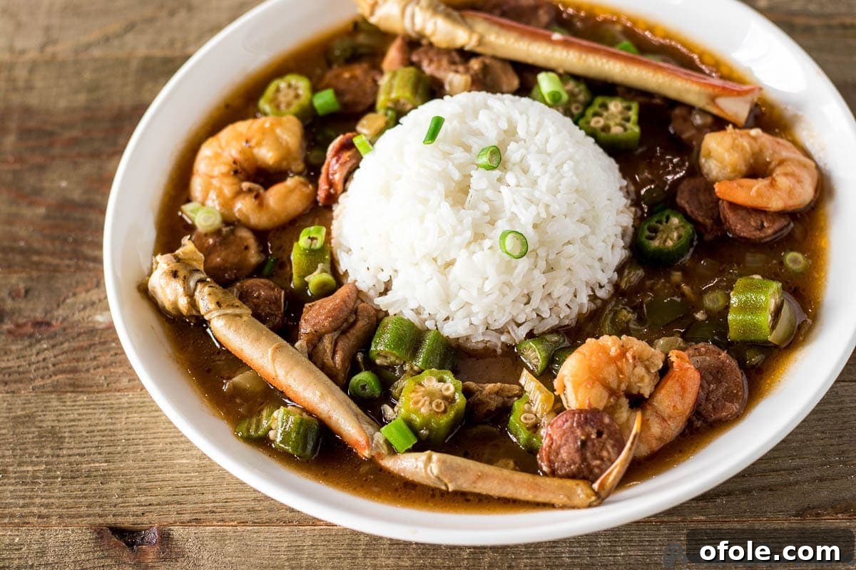 A large bowl of Seafood Gumbo, garnished with fresh green onions, featuring visible shrimp and crab legs, served alongside a portion of white rice.