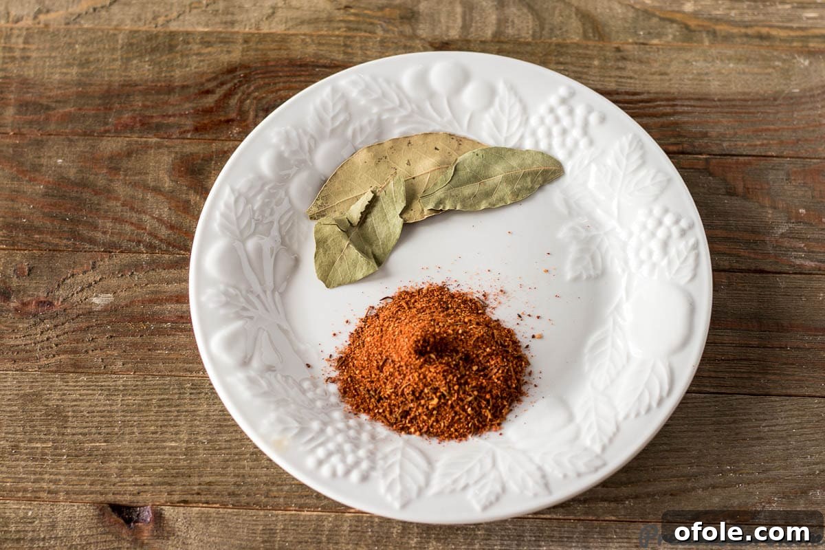 A small plate showcasing bay leaves and a spoon full of vibrant Creole seasoning, essential spices for an authentic gumbo.