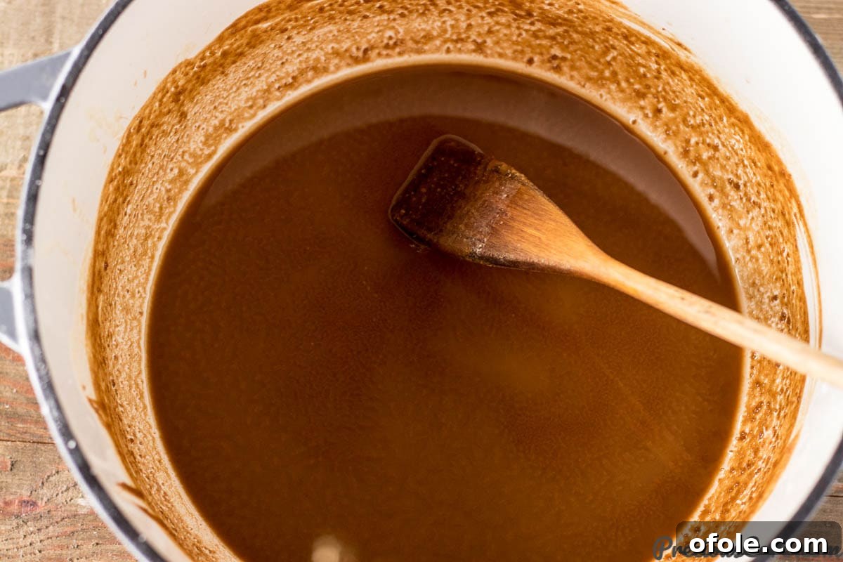 A wooden spoon stirring a rich, dark brown roux in a cast iron pot, showcasing the crucial base for gumbo.