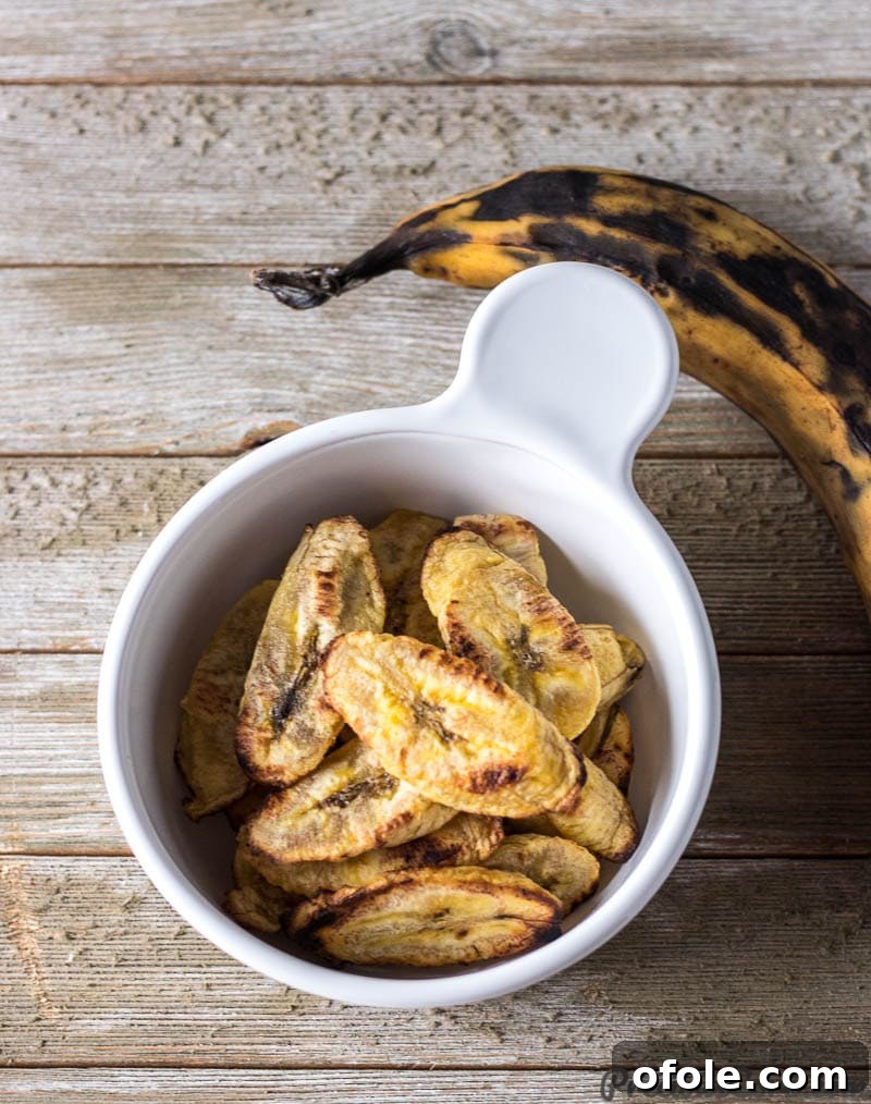 A bowl of baked plantains next to a whole uncooked ripe plantain, showcasing the raw ingredient.