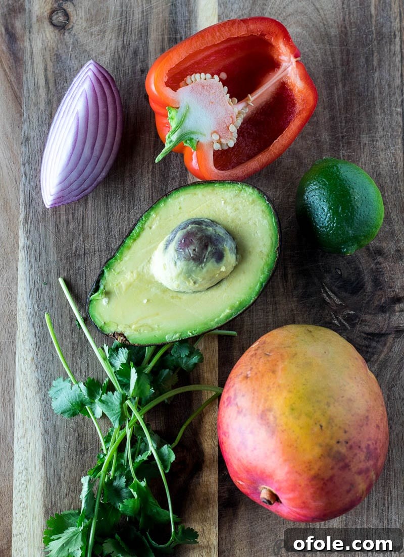 Red onion, red bell pepper, lime, avocado, cilantro, and mango on a chopping board for salsa.