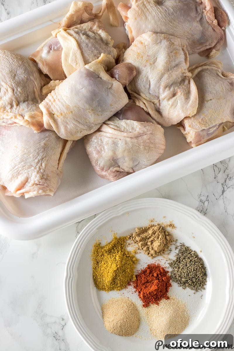 Golden Crispy Oven Chicken Thighs 3 Dry rub ingredients on a plate and raw chicken thighs on a tray