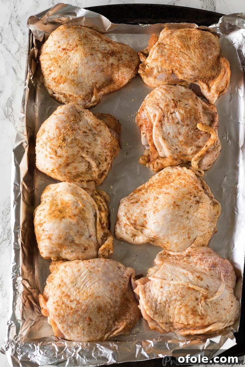 Golden Crispy Oven Chicken Thighs 4 chicken thighs in a baking sheet with spices rubbed all over them