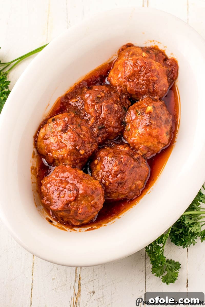 Savory Chicken Bites 4 Succulent baked chicken meatballs nestled in a vibrant, homemade tomato sauce within a stylish serving bowl, garnished with fresh basil.