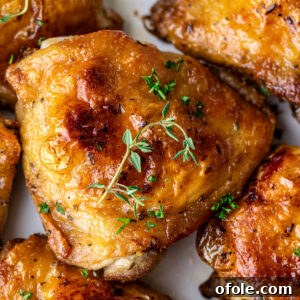 Close up on a golden brown chicken thigh, surrounded by other chicken thighs, juicy and delicious.
