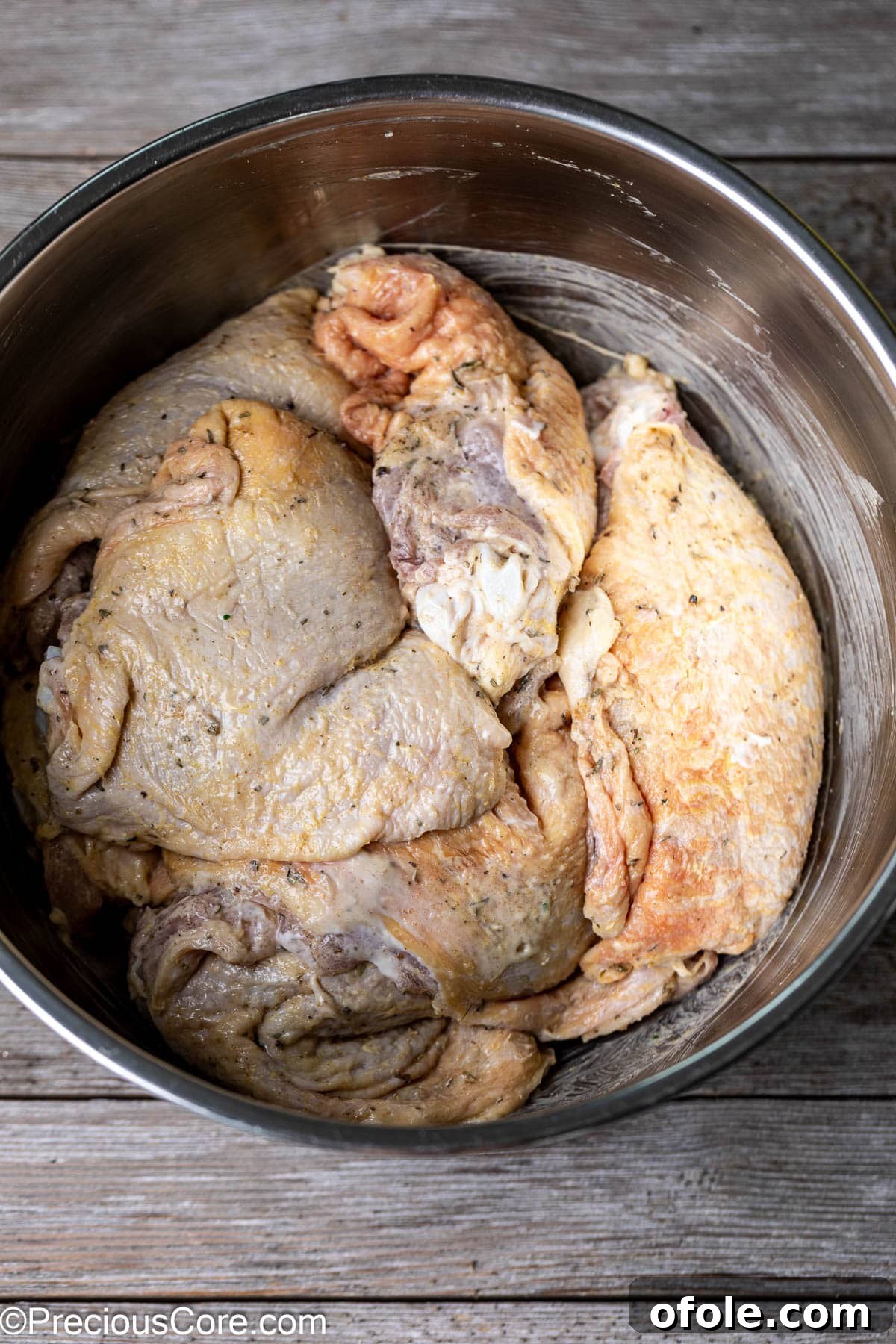 Seasoned chicken thighs in a stainless steel mixing bowl, thoroughly coated with the mayonnaise marinade.