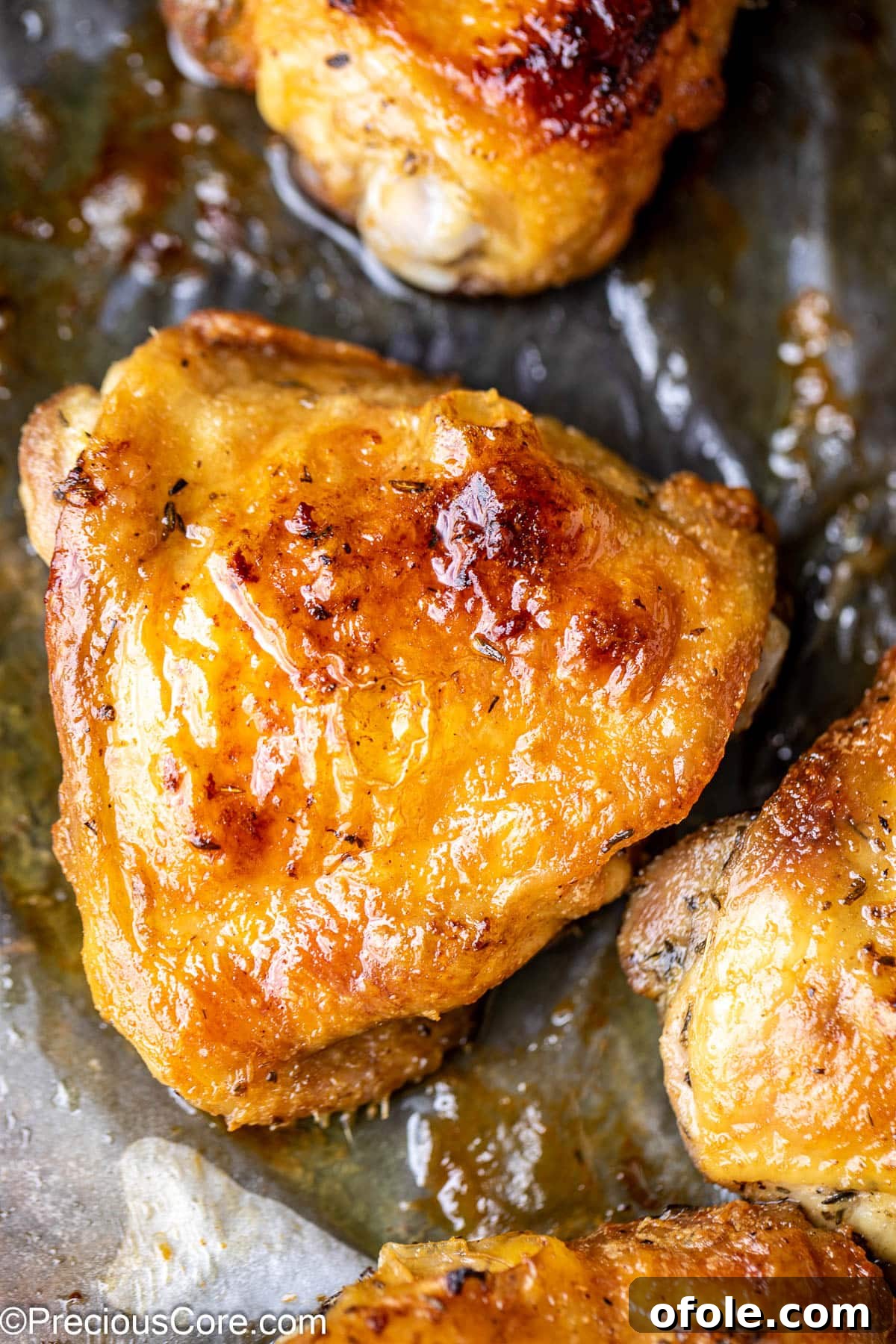 Close up on a glistening golden brown chicken thigh on parchment paper, ready to be served.