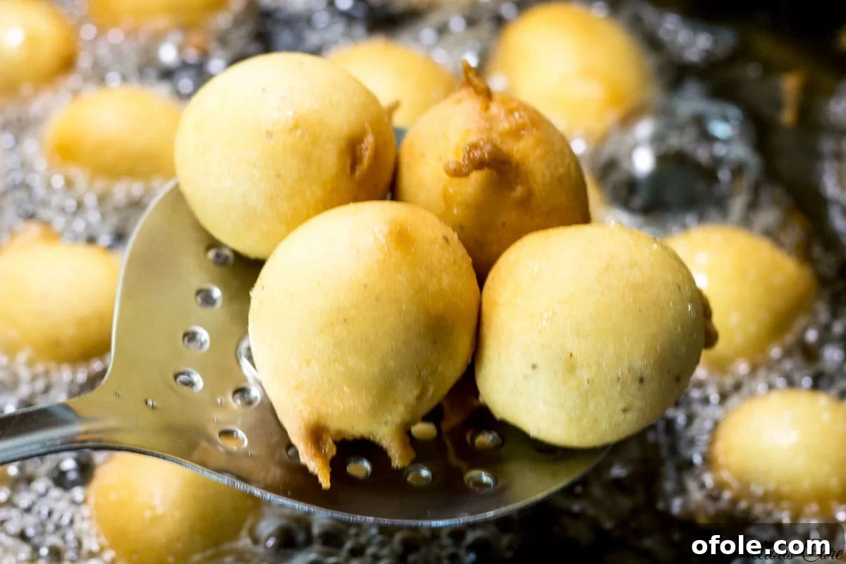 Frying spoon lifting golden brown Cameroon doughnuts from oil.