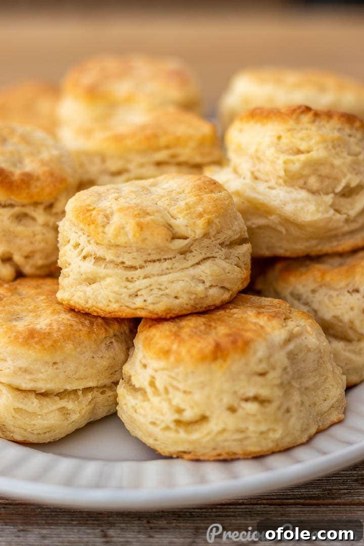 Stacked golden brown buttermilk biscuits on a white platter, showcasing their flaky layers and inviting texture.