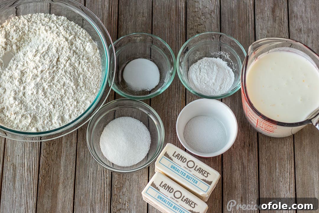 Close-up of fresh ingredients: butter, flour, buttermilk, baking powder, baking soda, salt, and sugar laid out for homemade buttermilk biscuits.
