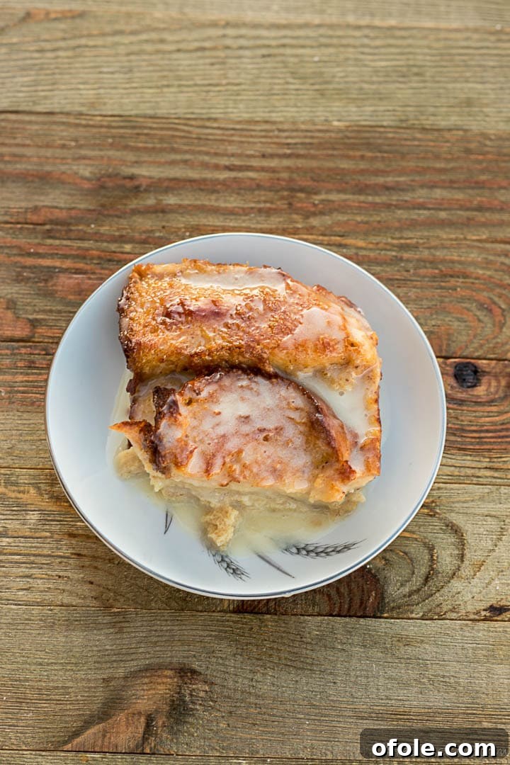 Golden Challah Bread Pudding 11 Individual serving of Challah Bread Pudding on a white dessert plate, with extra sauce