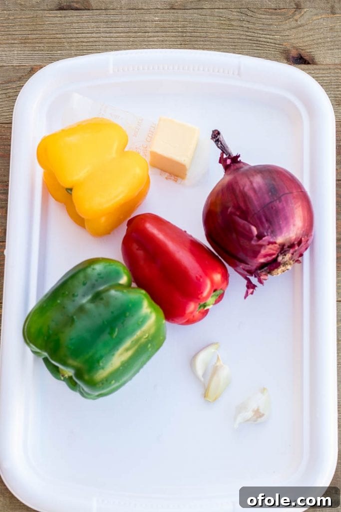 Assortment of fresh, colorful bell peppers (red, yellow, green) neatly arranged on a tray with whole onions and garlic cloves, ready for preparation.