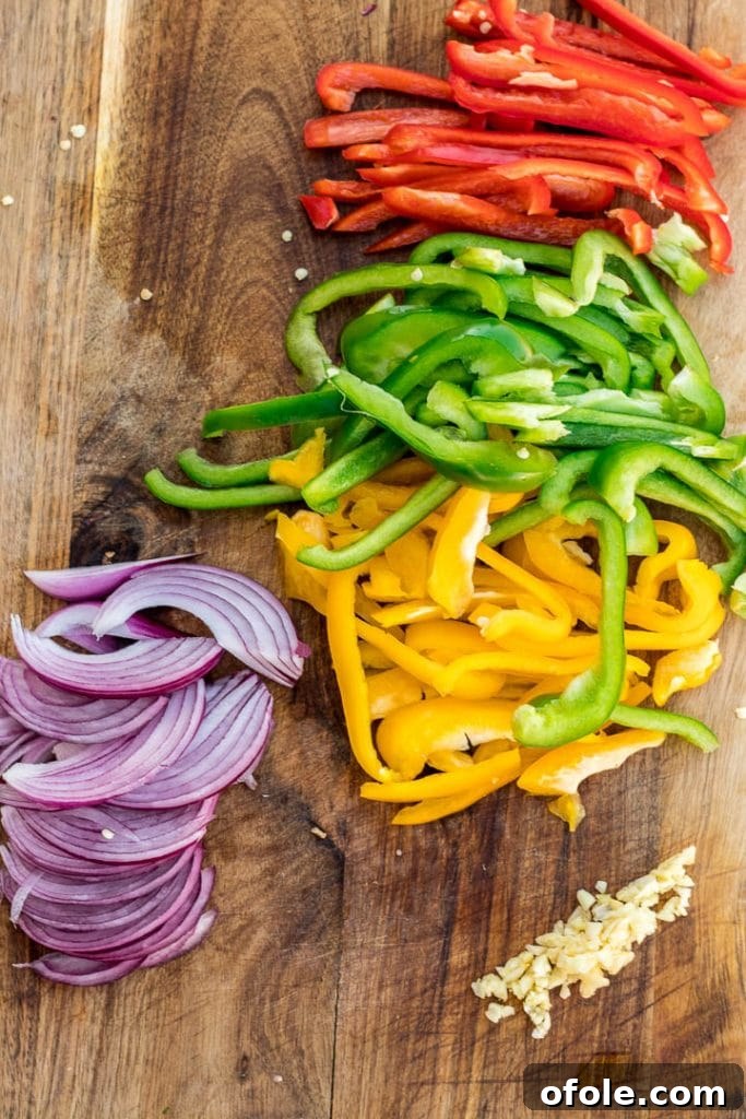 Sliced red, yellow, and green bell peppers neatly arranged on a chopping board alongside freshly minced garlic, ready for cooking.