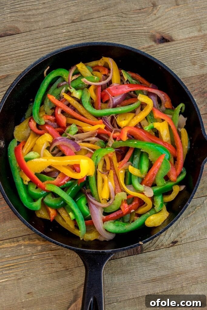 Colorful bell pepper and onion strips actively sauteing in a skillet, showing early stages of softening and caramelization.